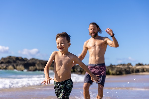 Dad and his kid run through the water on a Gold Coast beach